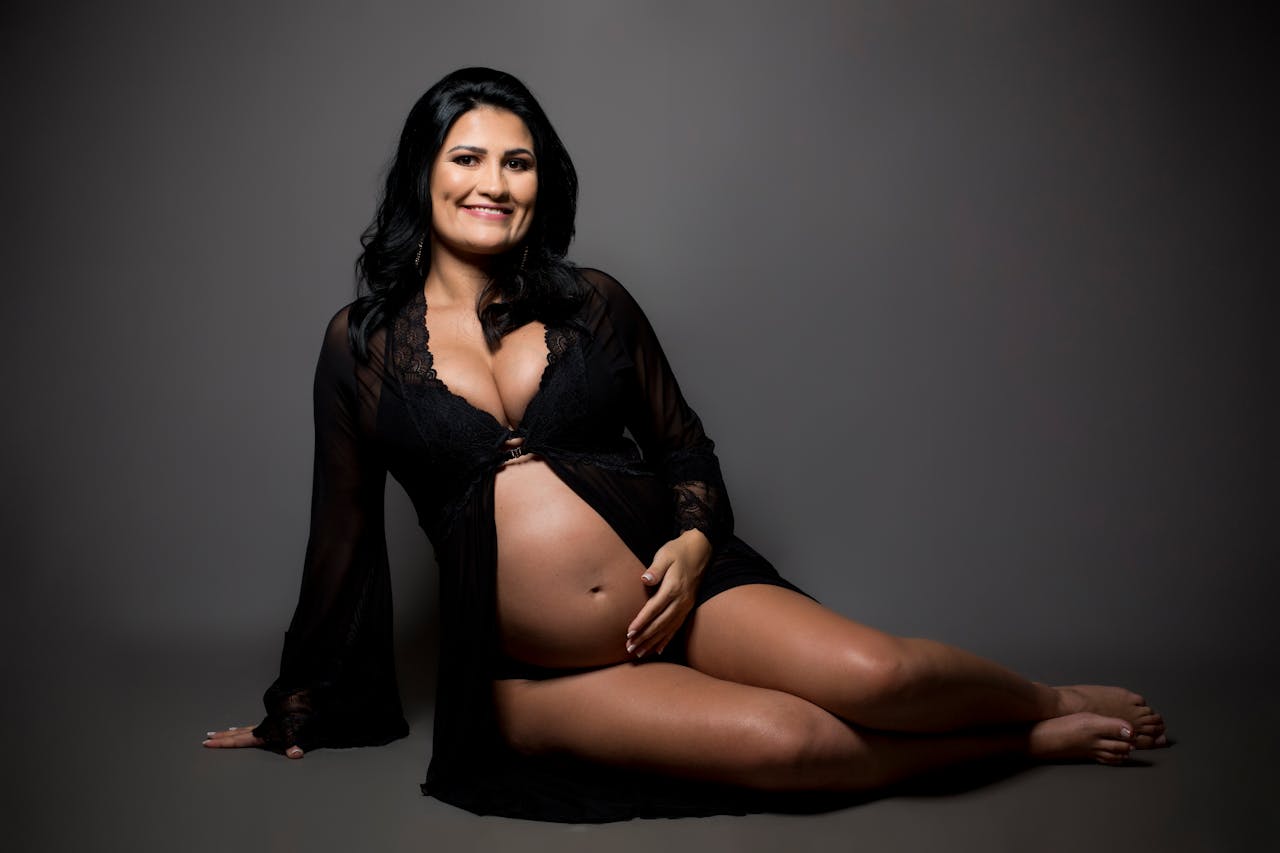 A serene studio portrait of a smiling pregnant woman in elegant maternity wear.