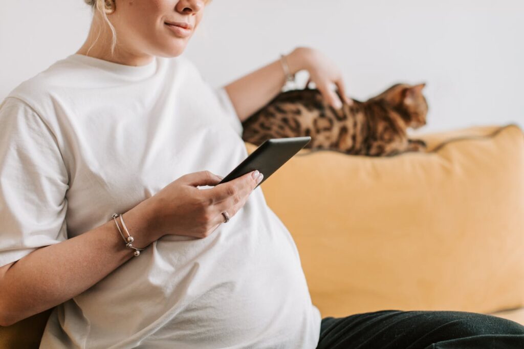 pexels-photo-8359707 A pregnant woman sitting indoors, using a smartphone, with a cat on the sofa.