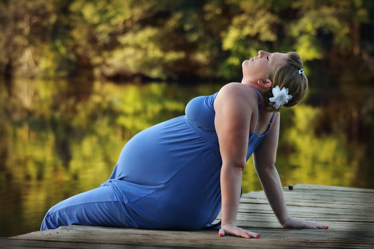 A pregnant woman on a pier by a lake, enjoying the outdoors while prioritizing ACOG sunscreen pregnancy advice.
