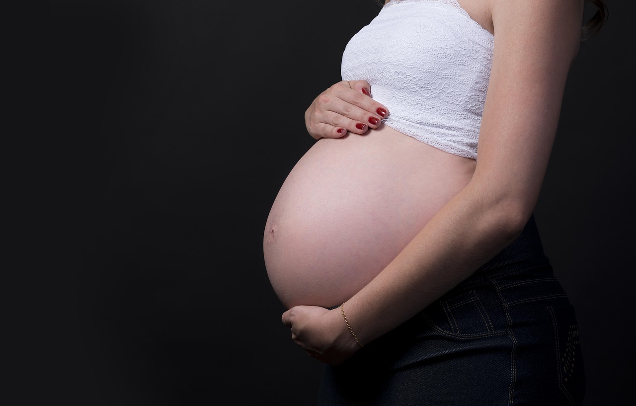 A pregnant woman gently cradles her prominent belly, representing safe vitamin and supplement choices during gestation.