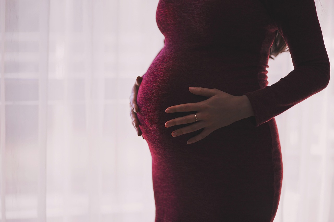 A pregnant woman gently touches her belly, illustrating the importance of pregnancy-safe mineral sunscreen.