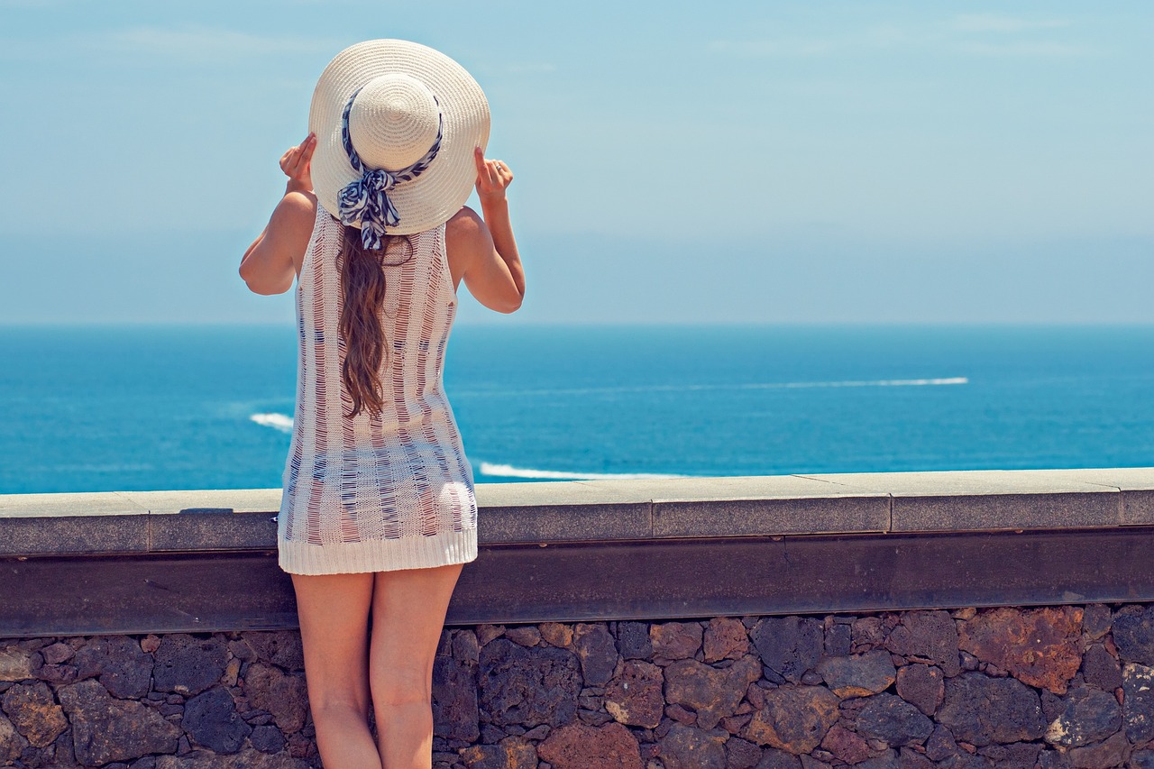 Woman in a sun hat on a sunny blue beach, enjoying the sun safely with mineral sunscreen for pregnancy.