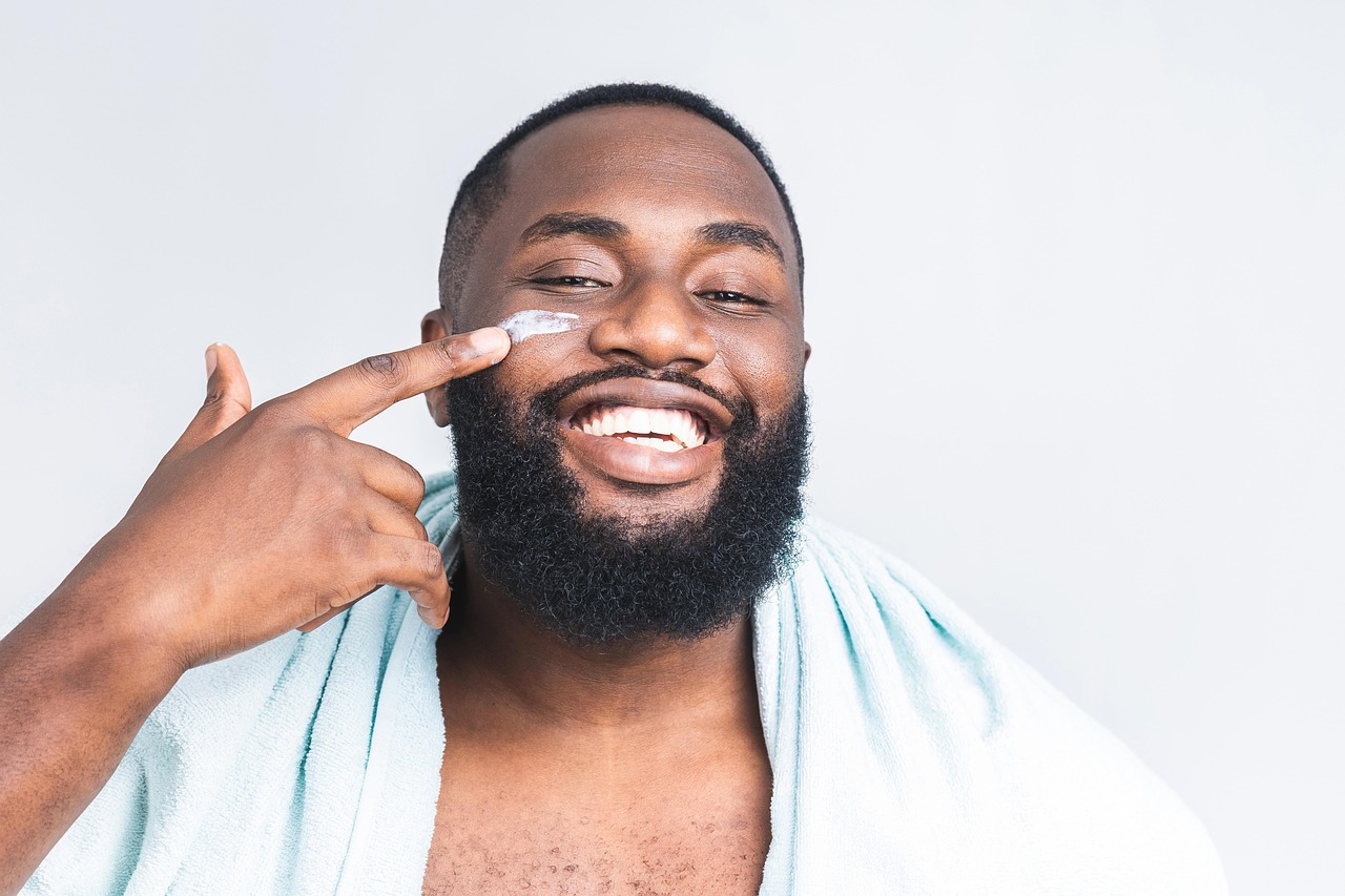A man with an afro applies face lotion, comparing popular pregnancy-safe skincare brands.