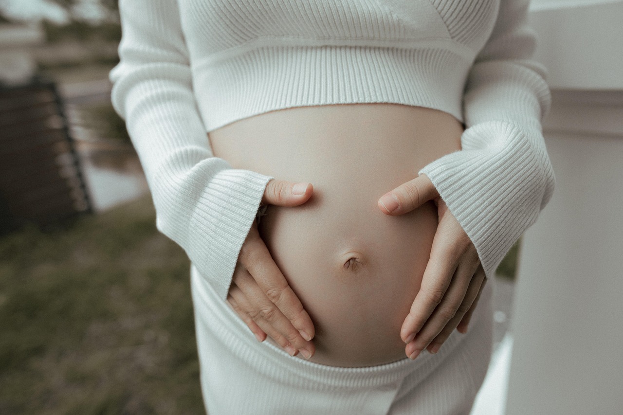 Pregnant woman's hands gently cup her belly, emphasizing mineral SPF and sun protection for healthy pregnancy skin.
