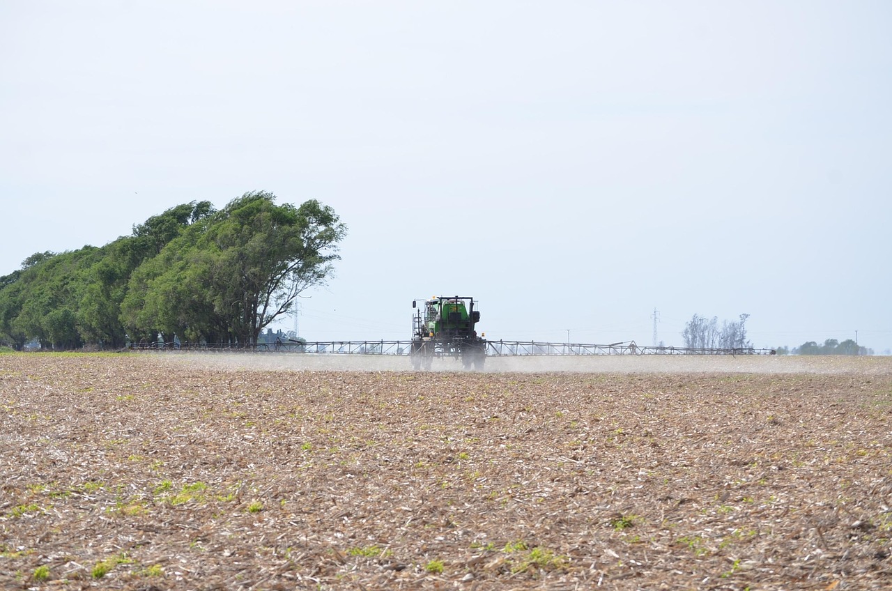 A large agricultural machine sprays a wide field, emphasizing the importance of broad protection like pregnancy safe sunscree