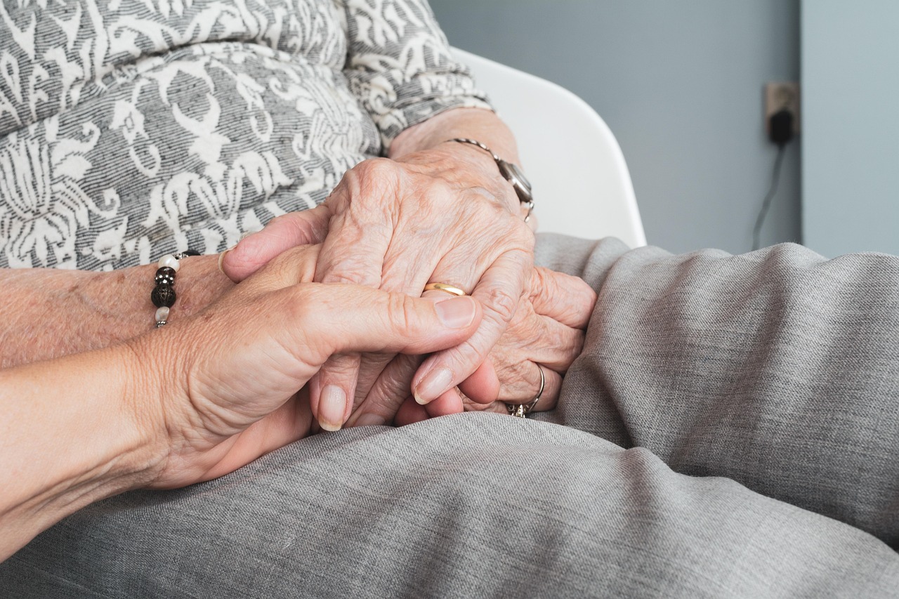 A wrinkled hand gently clasps another, symbolizing the care and support for expecting parents preparing for baby.