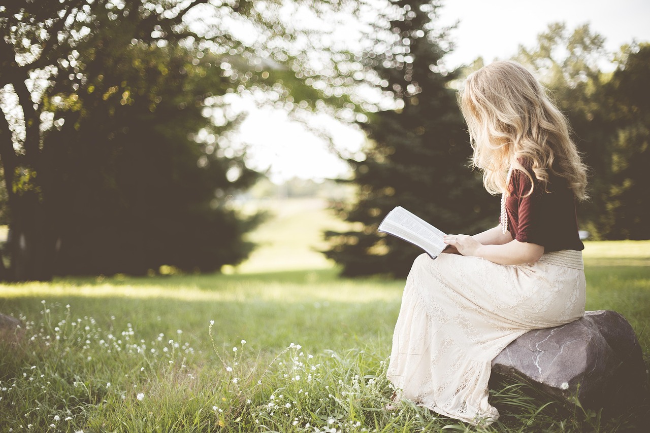 Blonde woman reads a book on the grass, navigating skincare choices like retinol during pregnancy.