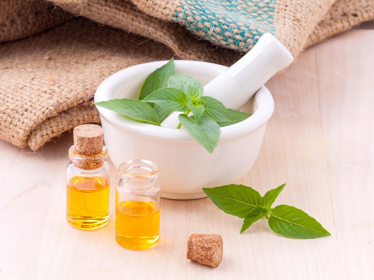 Mortar with fresh basil leaves and small bottles of natural oils on a wooden table, representing natural ingredients that can be risky