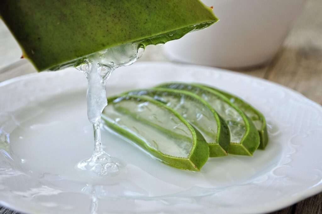 Sliced aloe vera leaf releasing clear gel onto a white plate, representing aloe vera for stretch marks