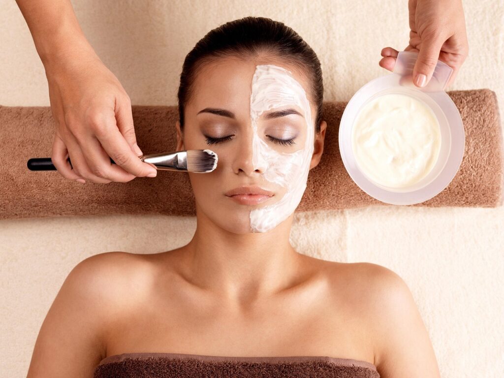 Woman relaxing while a therapist brushes a white facial treatment onto half her face, representing chemical peels