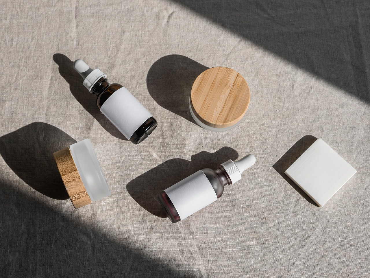 Amber dropper bottles, a bamboo-lid jar and small bottles arranged on linen in sunlight, representing bakuchiol serums compared