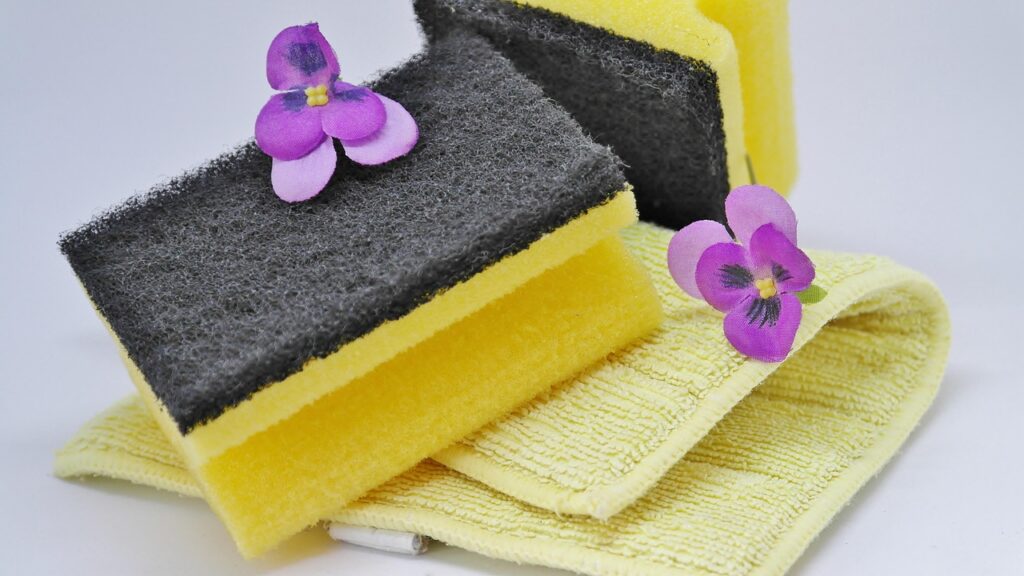 Yellow cleaning sponges with purple flowers beside a washcloth, suggesting face washing and acne cleanser routines for benzoyl peroxide