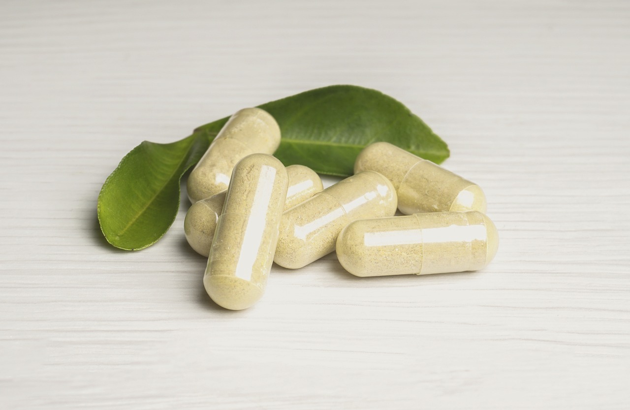 Vitamin capsules beside a green leaf on a white surface, representing pregnancy vitamins and supplements