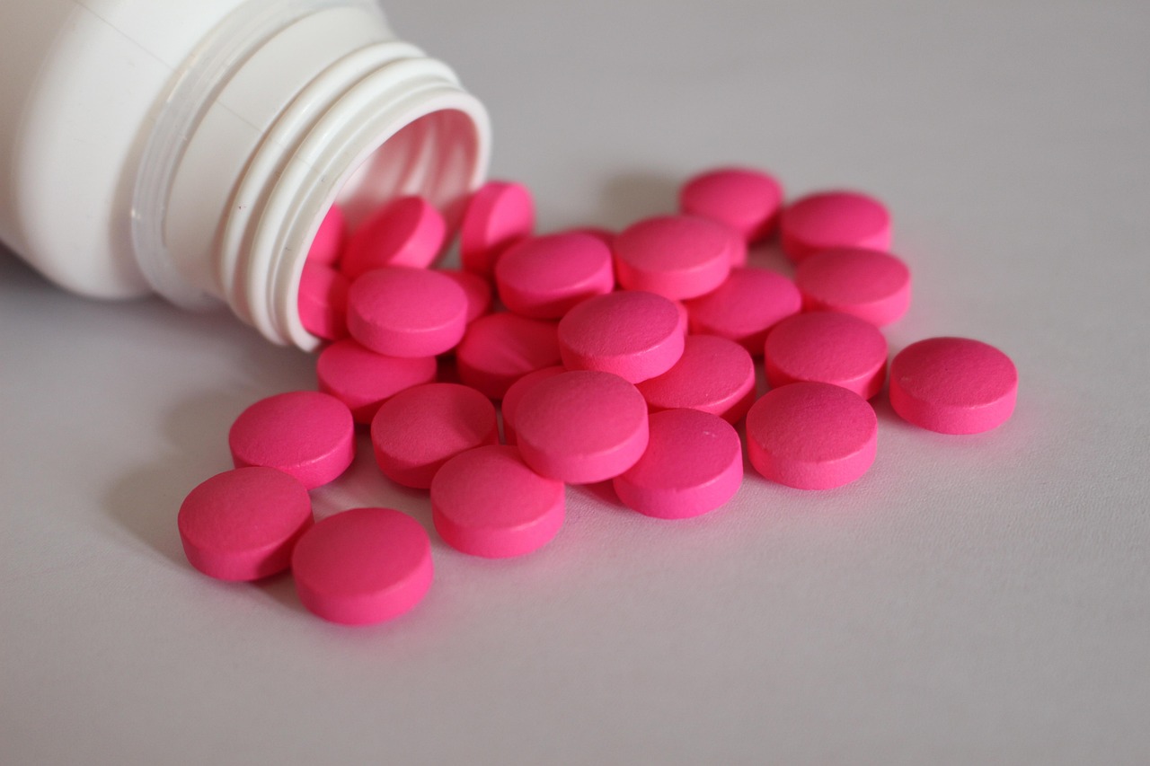 White bottle with pink ibuprofen-style painkiller tablets spilled on a gray surface, representing pain relievers in pregnancy
