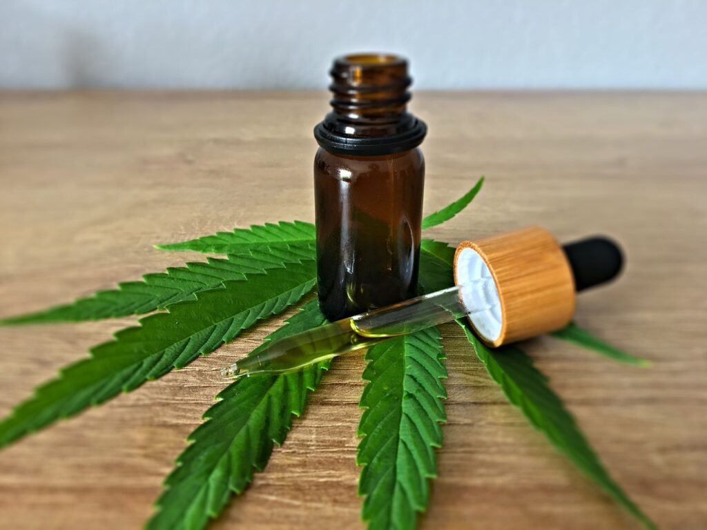 Amber dropper bottle of hemp-derived oil resting beside green hemp leaves on a wooden table