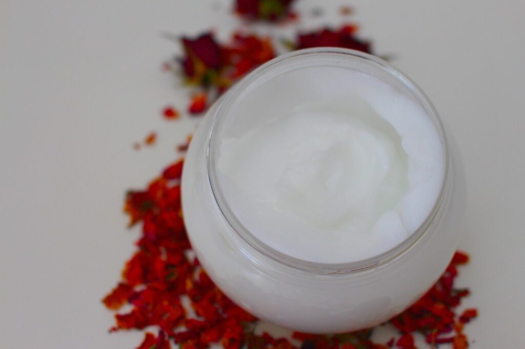 White moisturizing cream in a glass jar surrounded by dried rose petals, representing ceramide skincare