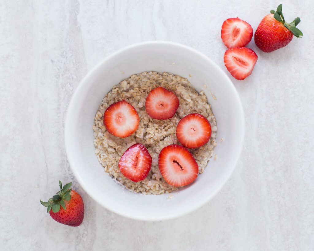 Bowl of plain oatmeal with sliced strawberries on a light surface, representing colloidal oatmeal
