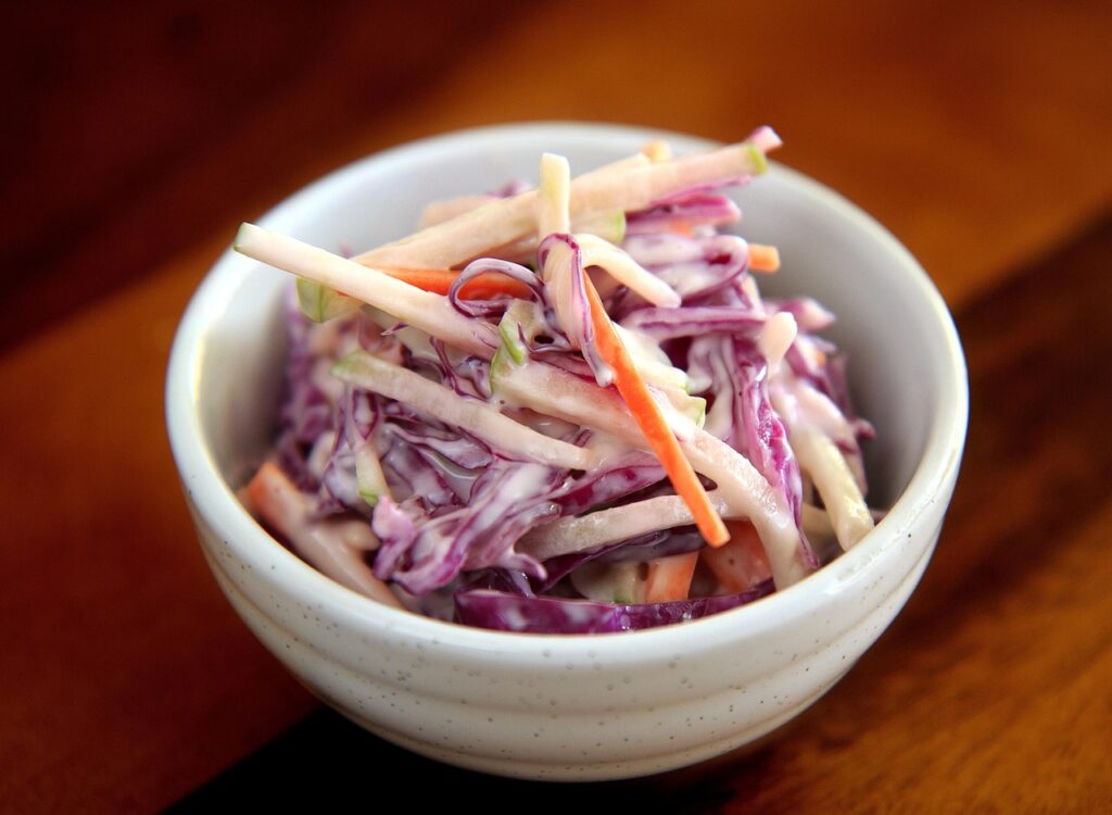 White bowl of creamy purple and white coleslaw with carrot strips, a typical premade deli salad in pregnancy