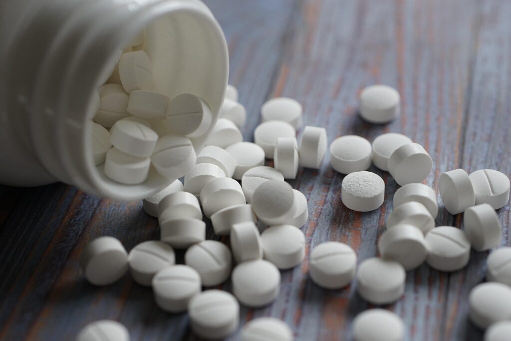 White tablets spilling from a tipped-over bottle onto a wooden table, representing an over-the-counter sleep aid for pregnancy nausea