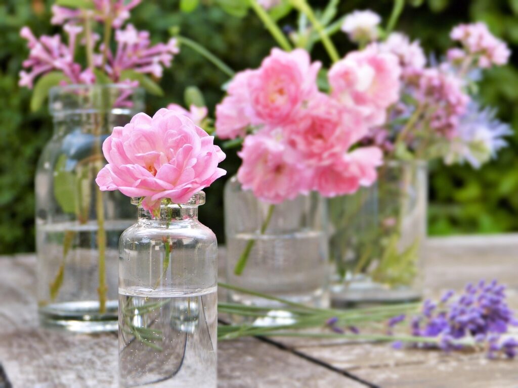 Small glass bottles and vials with pink blossoms and lavender sprigs on a table, representing essential oils in pregnancy