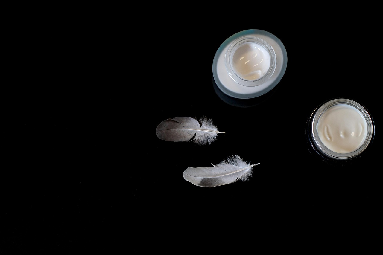 Two jars of moisturizing cream with white feathers on a dark surface, representing gentle skincare for expecting parents