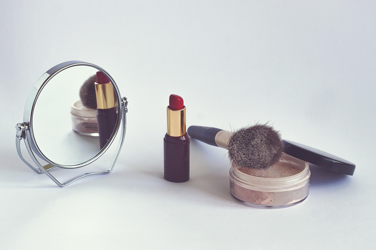 Lipstick, face powder, brush and a small standing mirror on a pale surface, representing a pregnancy cosmetic checker