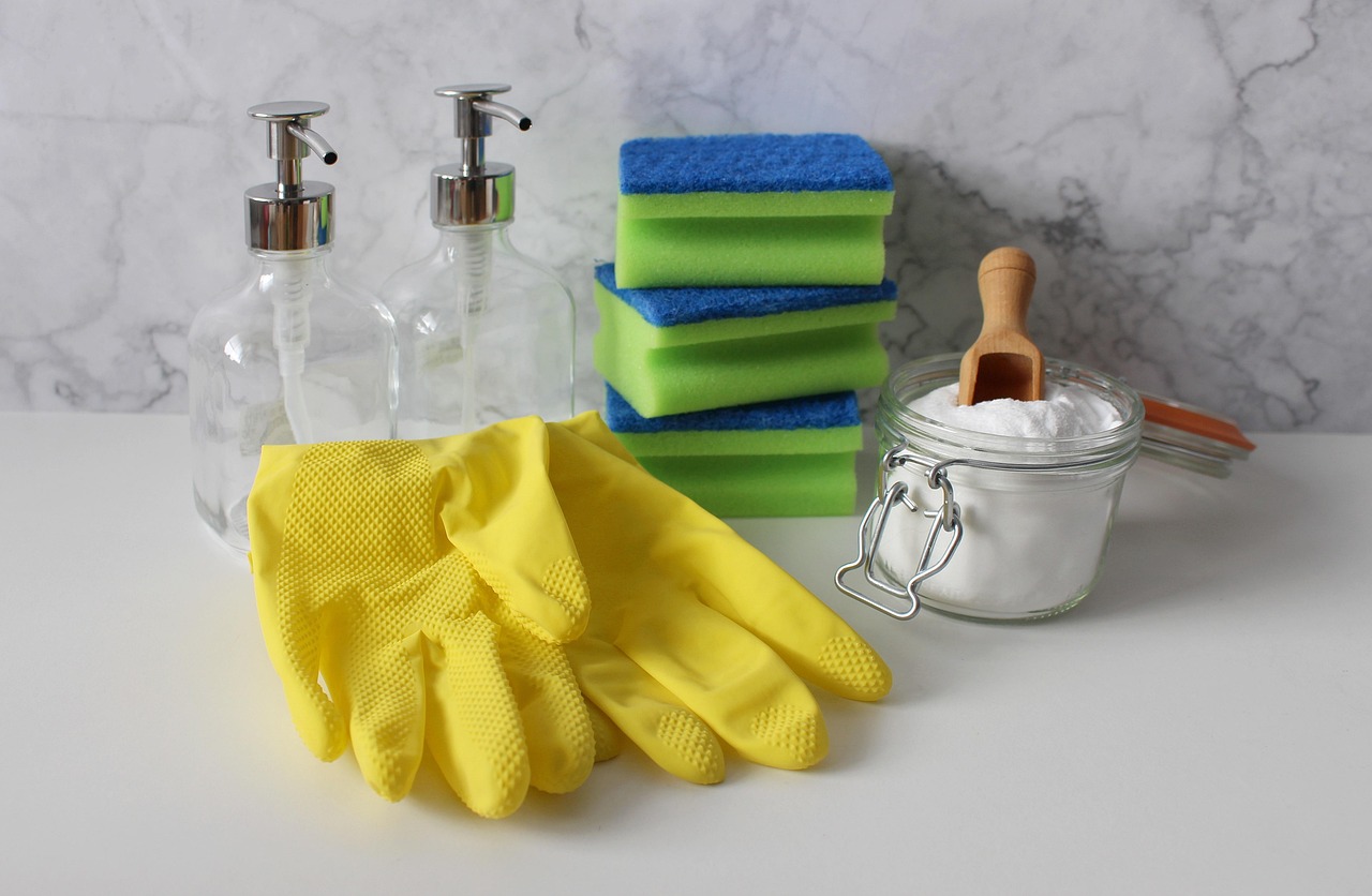 Yellow rubber gloves, sponges, soap dispensers and baking soda on a marble counter, representing household products to scan