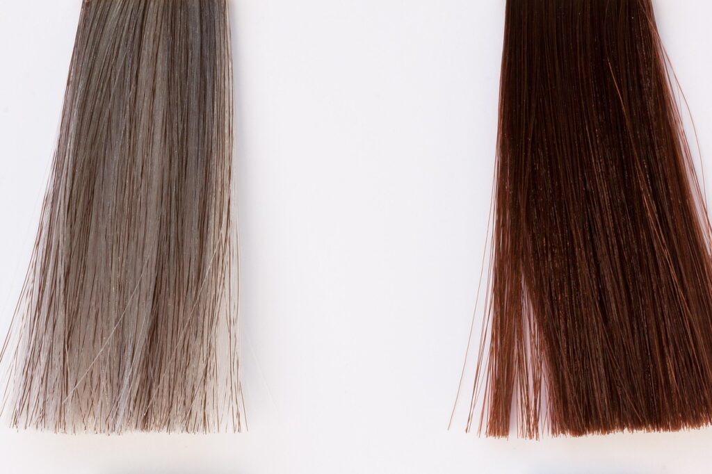 Two straight hair color sample strands, one blonde and one light brown, representing hair dye