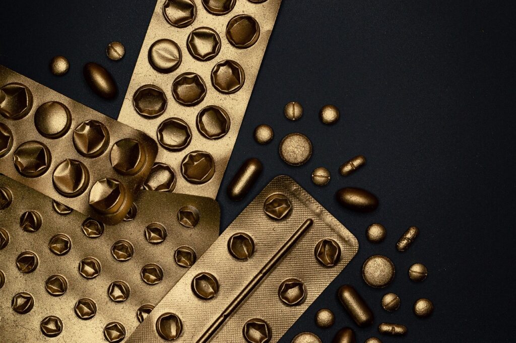 Gold-toned blister packs of pills scattered on a dark surface, representing high-dose vitamin A supplements