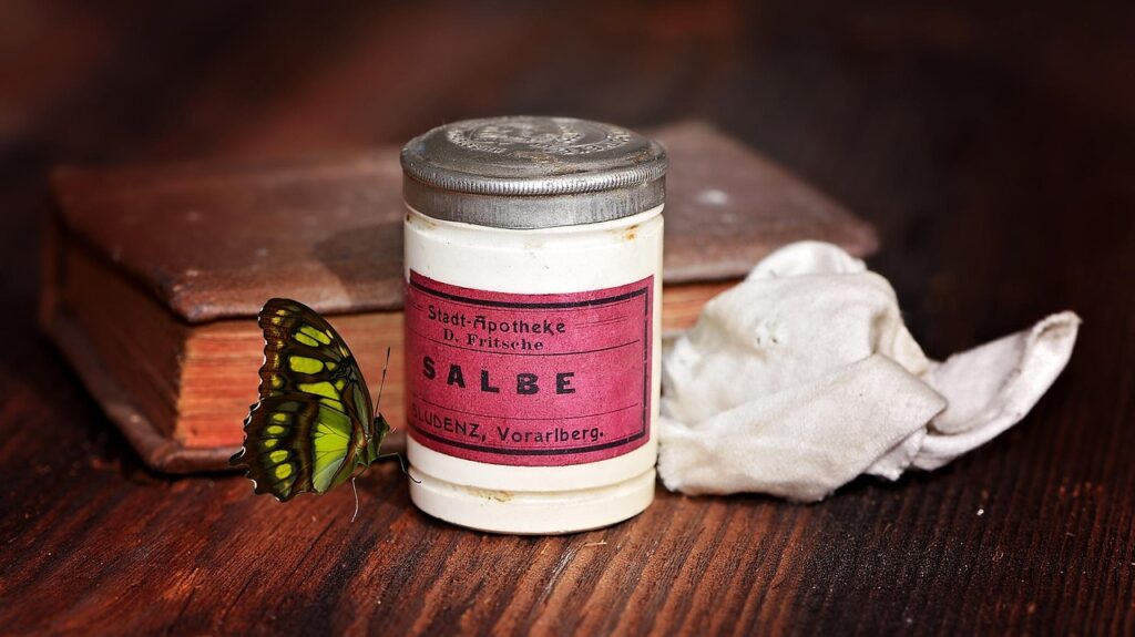Vintage tin of ointment beside an old book and cloth, representing topical creams such as hydrocortisone