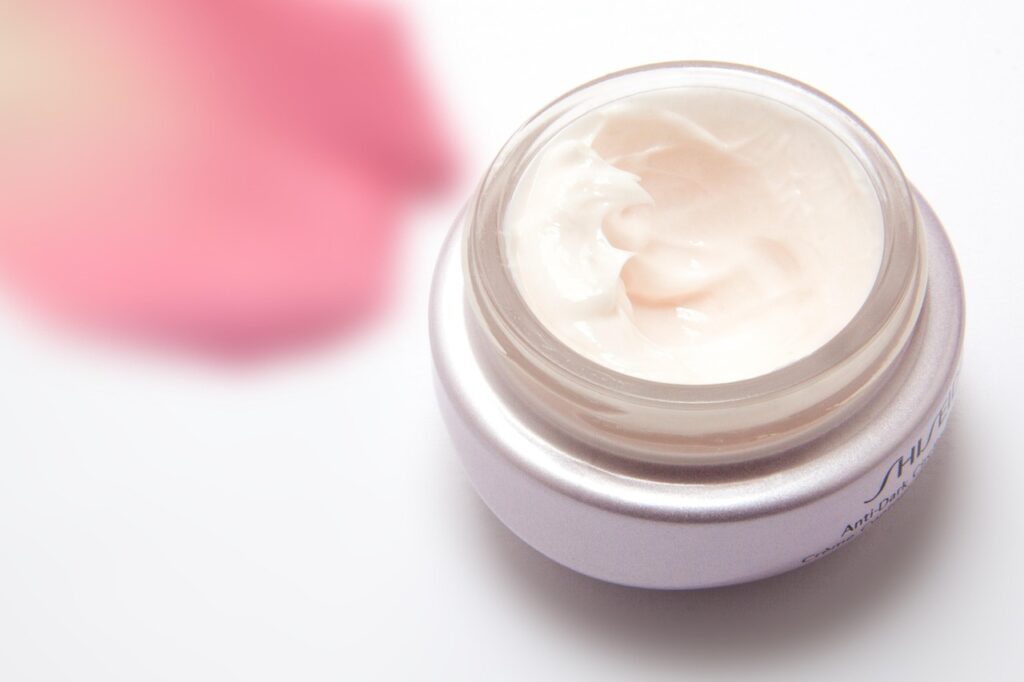 Jar of pink-tinted skin cream beside a rose, representing hydroquinone skin lightening cream