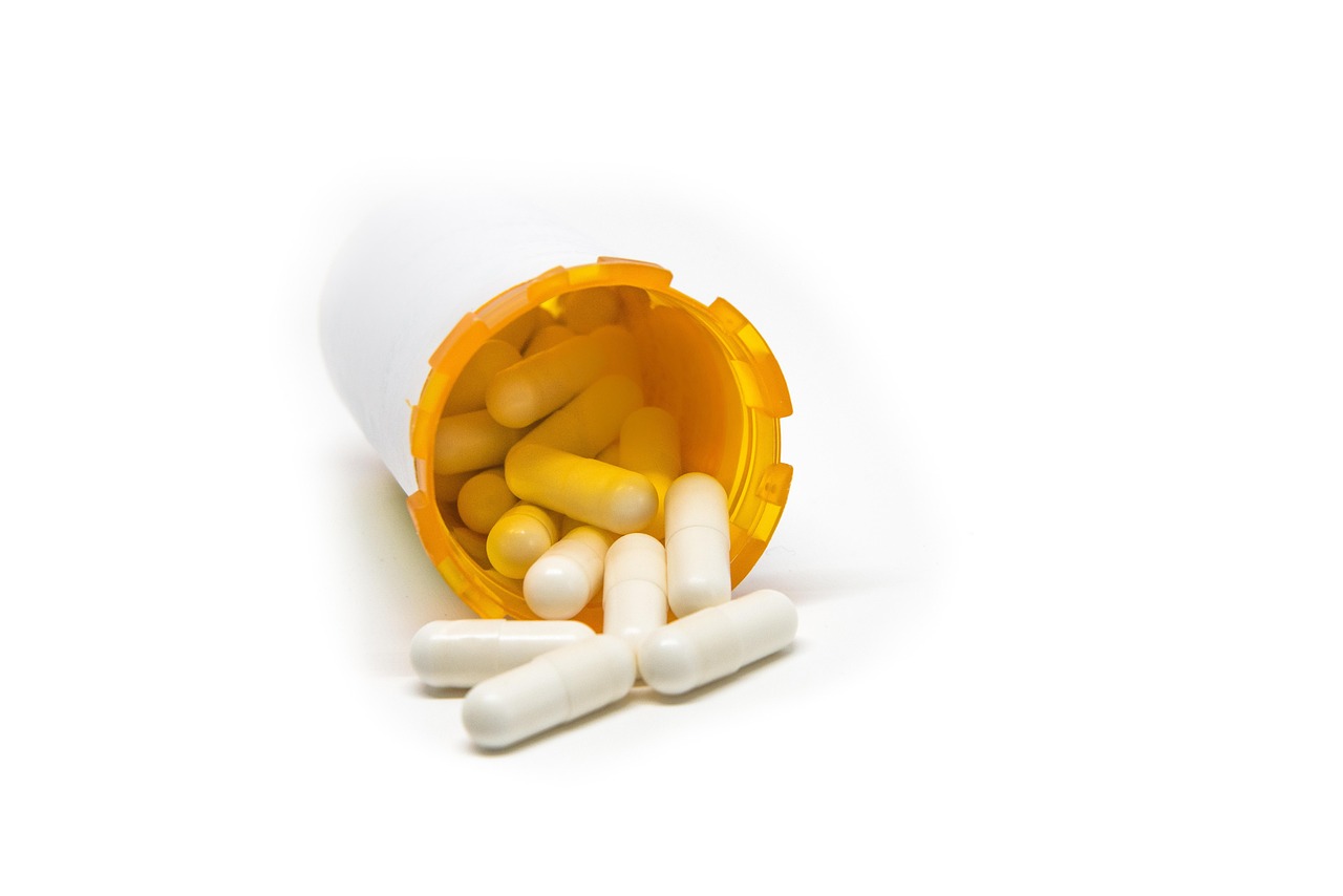 Orange supplement bottle tipped over with white capsules spilling out, representing iron pills