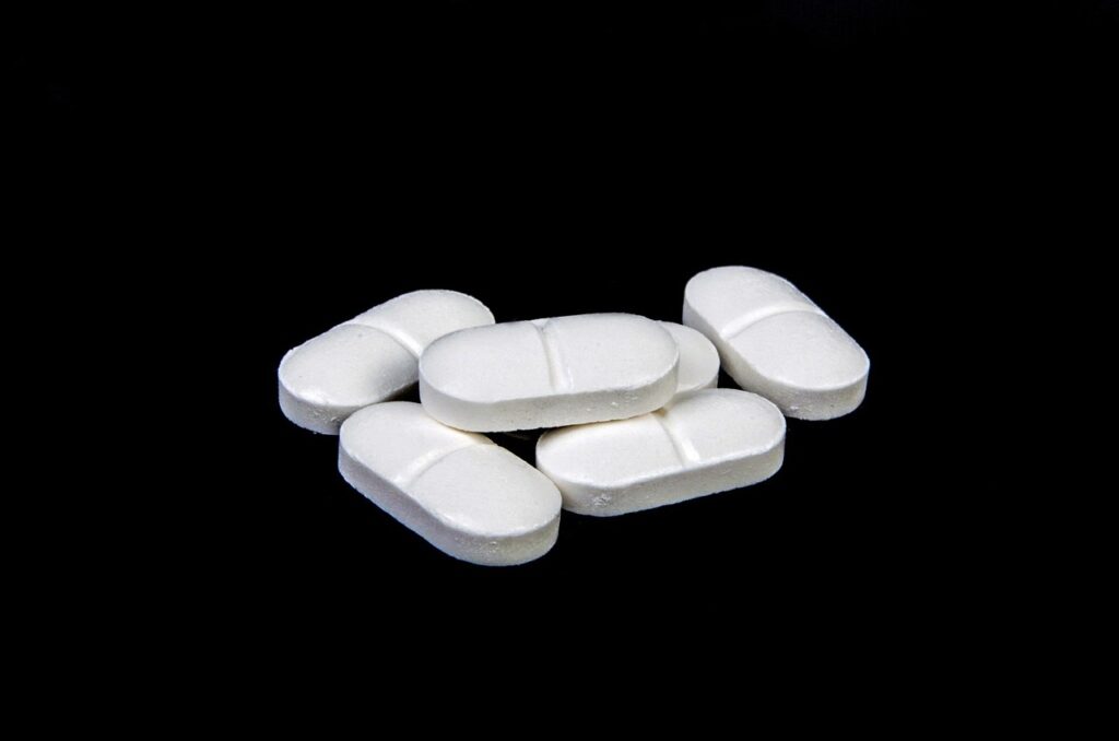Several white oblong tablets with score lines arranged on a black surface, representing aspirin