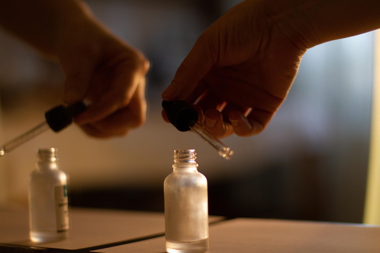 Hands holding a glass dropper above a small frosted serum bottle on a wooden table, representing a retinol serum