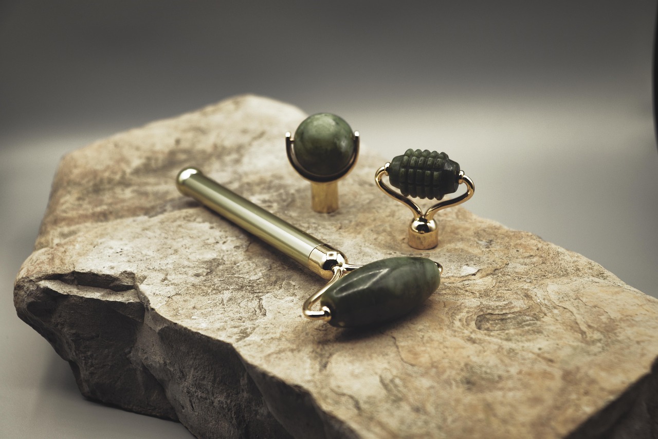 Jade face rollers with gold handles resting on a stone slab, representing a gentle bakuchiol retinol alternative skincare routine