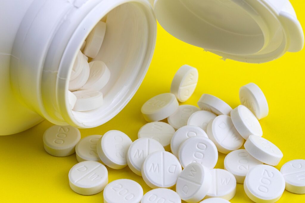 White tablets spilling from an open white bottle onto a yellow surface, representing ibuprofen