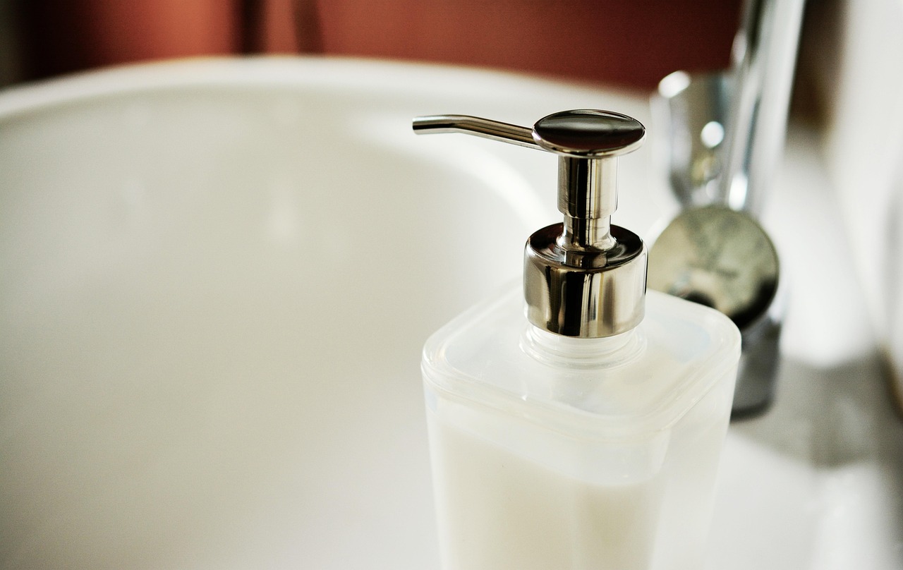 Liquid soap dispenser beside a bathroom sink, representing an acne foaming wash
