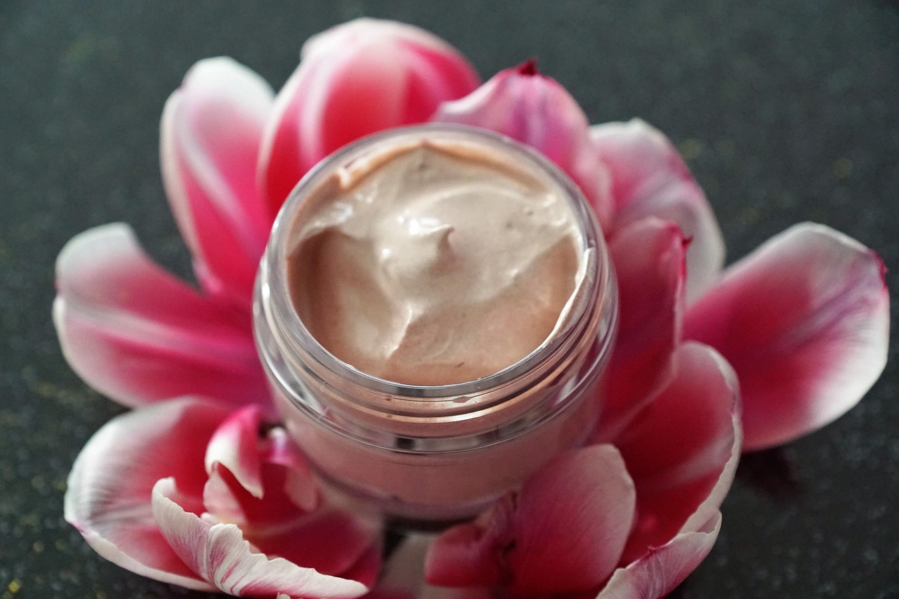 Jar of pale pink cream resting on pink flower petals, representing a prescription retinoid cream like Retin-A