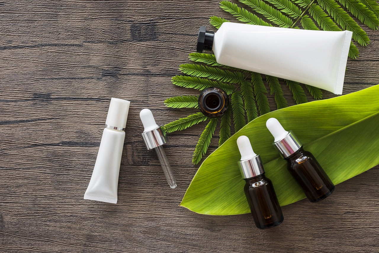White cosmetic tubes and dropper bottles on green leaves and wood, representing checking skincare app ingredients
