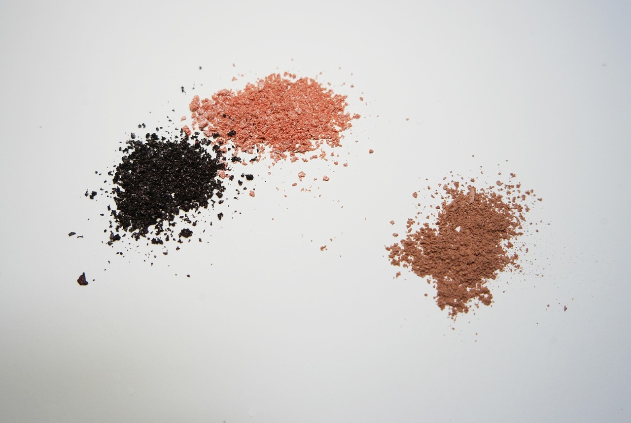 Small piles of pink, black and tan cosmetic powders on a pale surface, representing kojic acid skincare ingredients