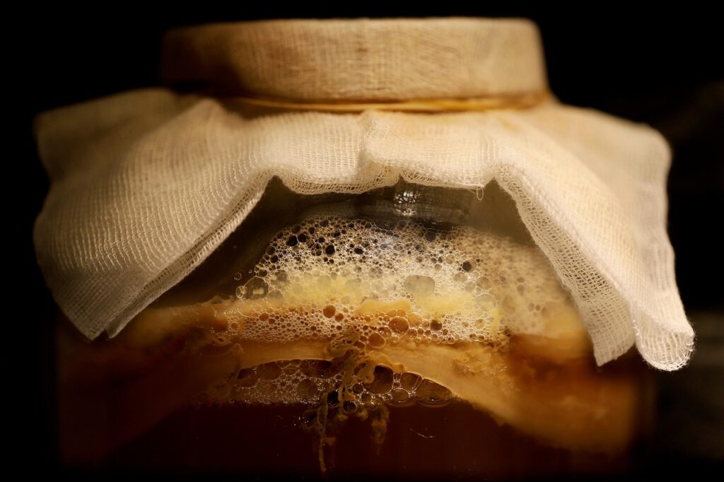 Glass jar of fermenting kombucha covered with cloth, foamy tea visible inside, for the kombucha in pregnancy question