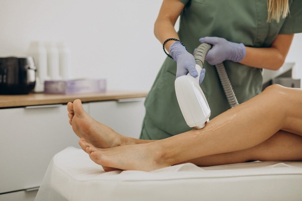 Technician in green scrubs and gloves using a laser device on a woman's leg, representing laser hair removal