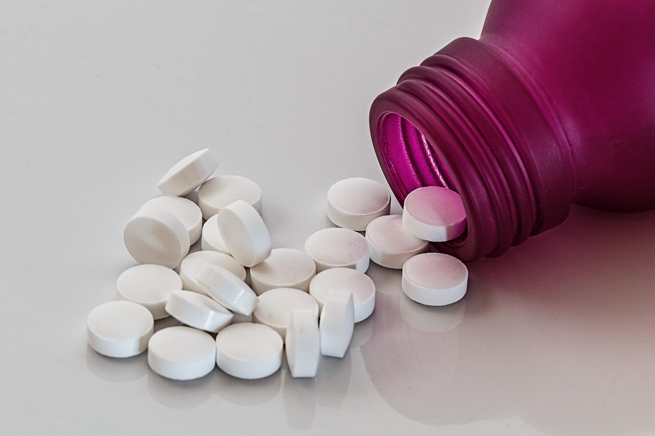 Magenta pill bottle tipped over with white tablets spilled on a grey surface, representing medication safety in pregnancy