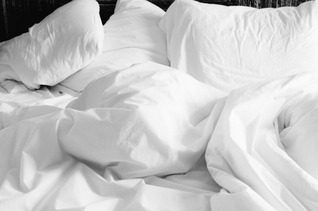 Rumpled white pillows and bed sheets, illustrating whether melatonin sleep aids are safe during pregnancy