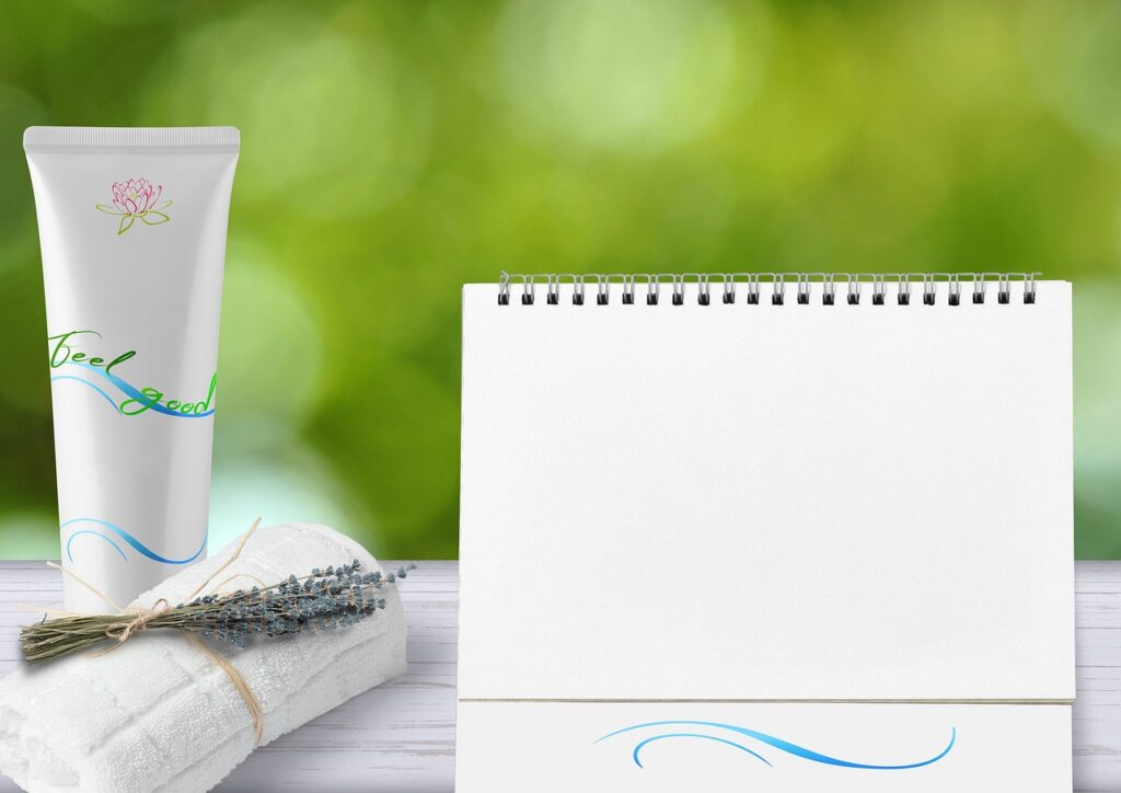 Plain white cream tube beside a lavender-tied towel and blank calendar on green, representing mineral sunscreen lotion in pregnancy