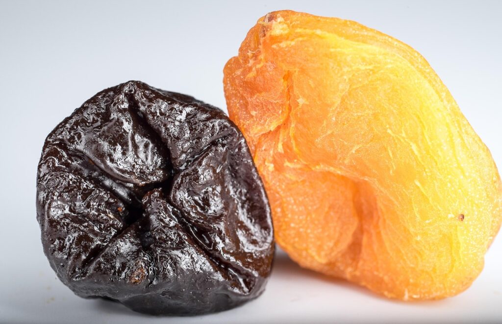 Dried prune and dried apricot on a white surface, natural foods often linked to constipation relief in pregnancy