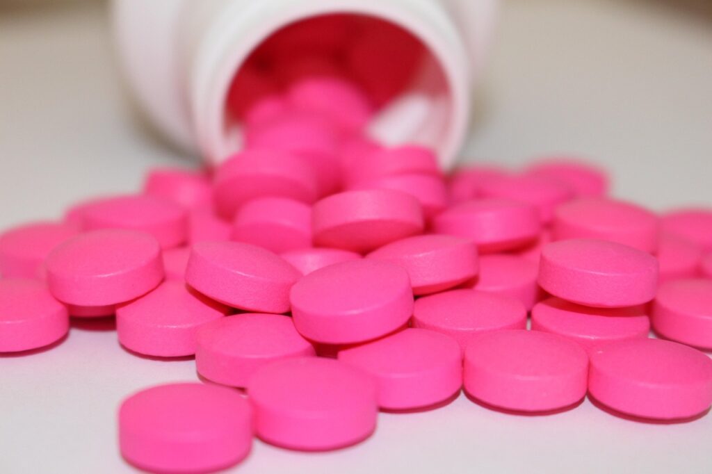 Pink round tablets spilling from a white bottle onto a light surface, representing an over-the-counter pain reliever