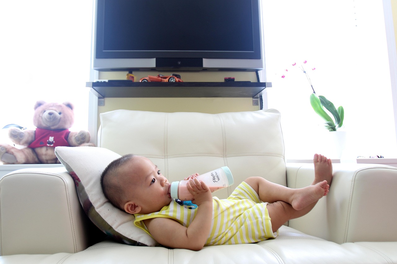 Baby lying on a white sofa drinking milk from a bottle, representing infant formula safety and recall awareness