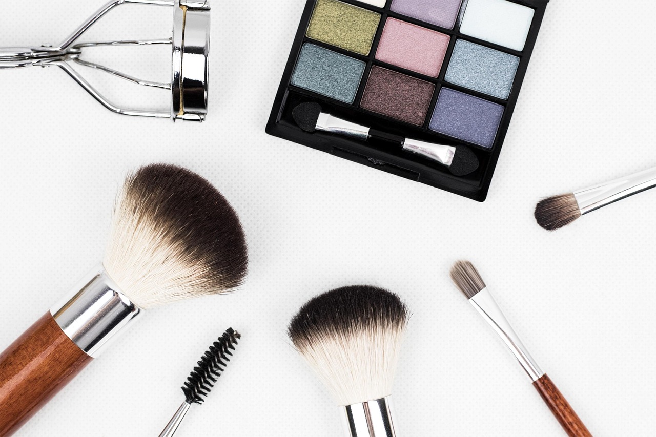 Makeup brushes, eyeshadow palette and eyelash curler on a white surface, representing checking cosmetics during pregnancy