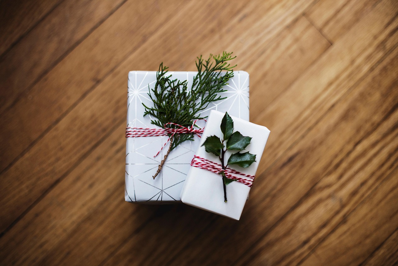 Two wrapped white gift boxes with green sprigs on a wooden table, representing holiday shopping for expecting parents